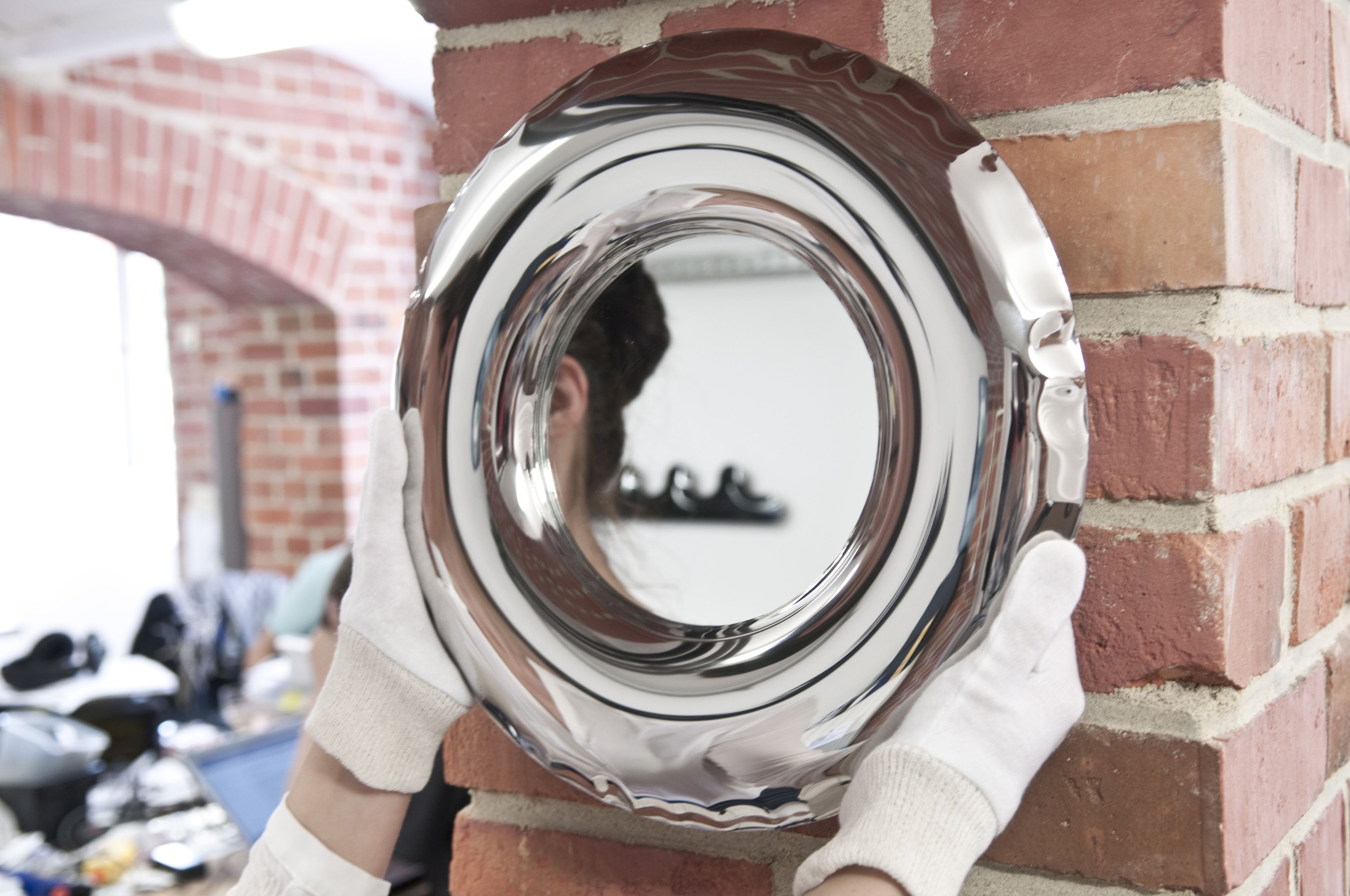 Rondel Spiegel aus Edelstahl von Zieta, gehalten von Händen mit weißen Handschuhen.
