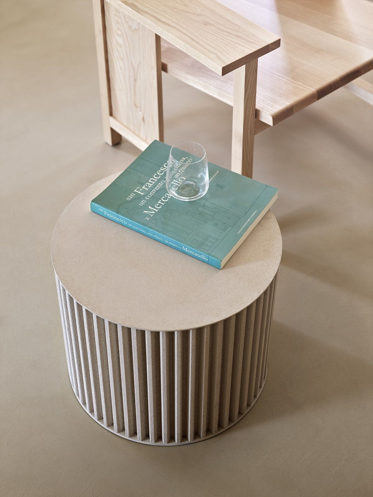Herclino Couchtisch: Runder Beistelltisch in Beige mit geriffelter Oberfläche, Buch und Glas.