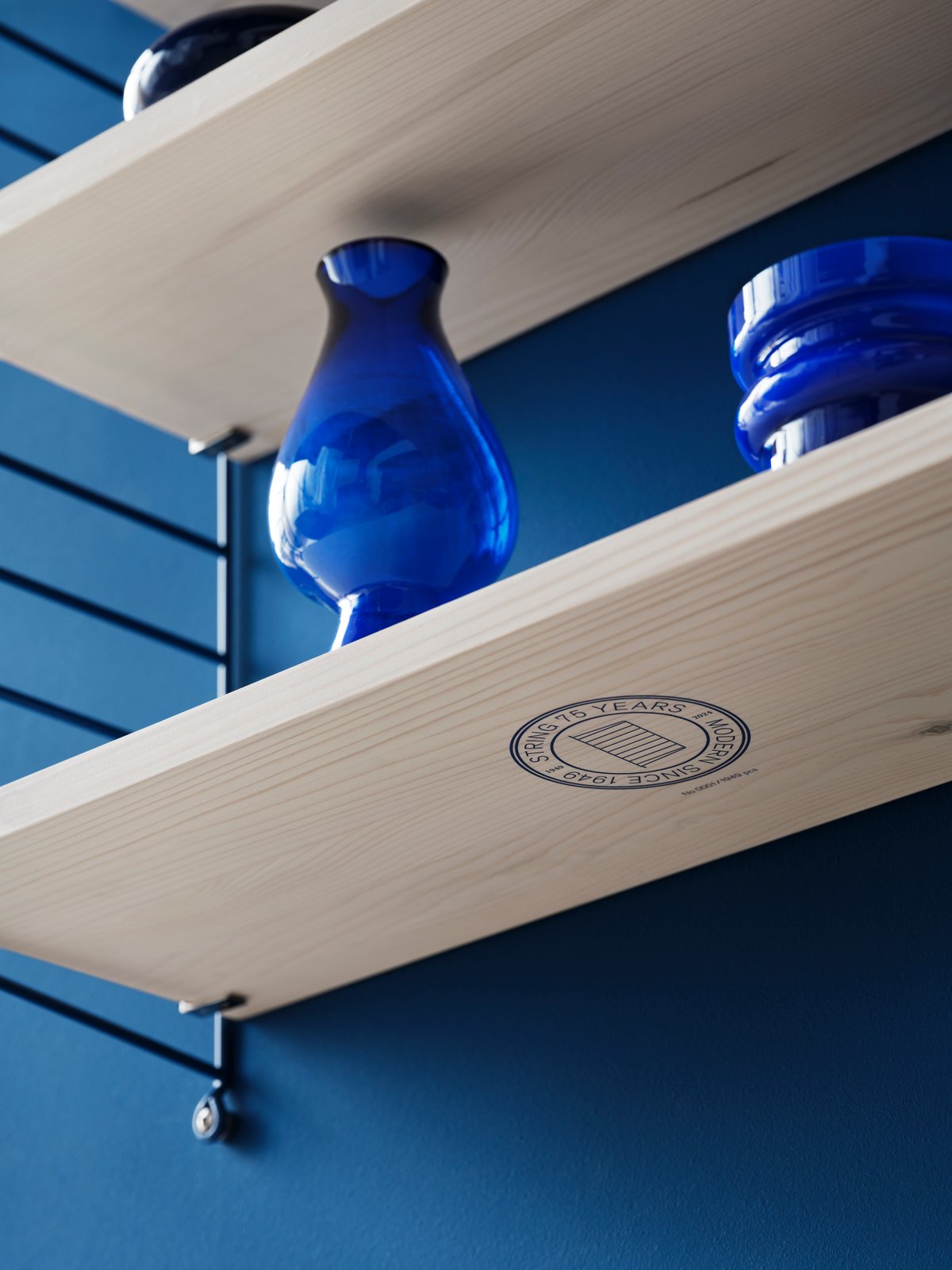 Detailaufnahme: String Regalbrett der Limited Edition mit blauen Glasvasen vor blauer Wand.