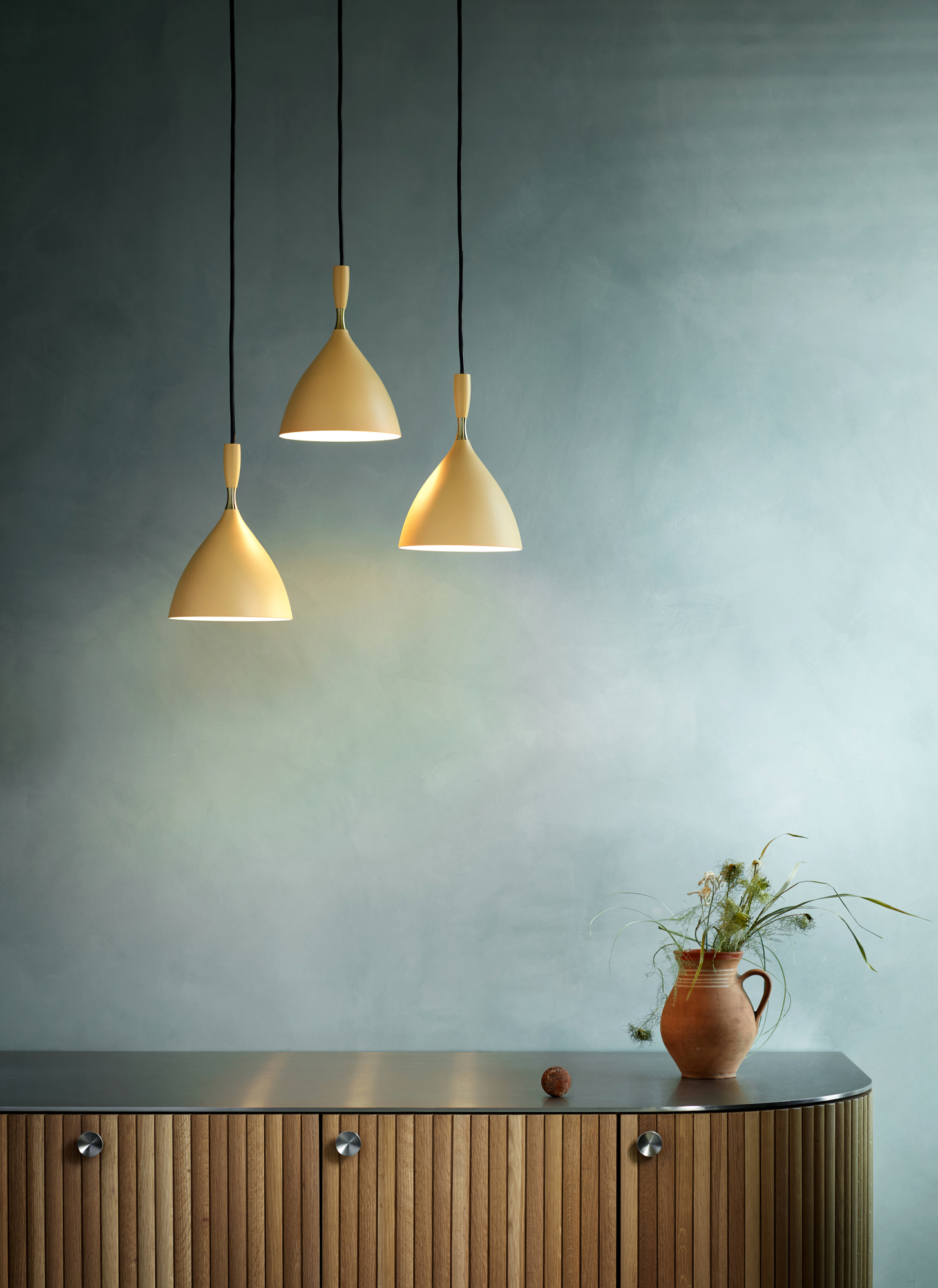 Drei gelbe Dokka Pendelleuchten von Northern hängen über einem Holzschrank mit Blumenvase.