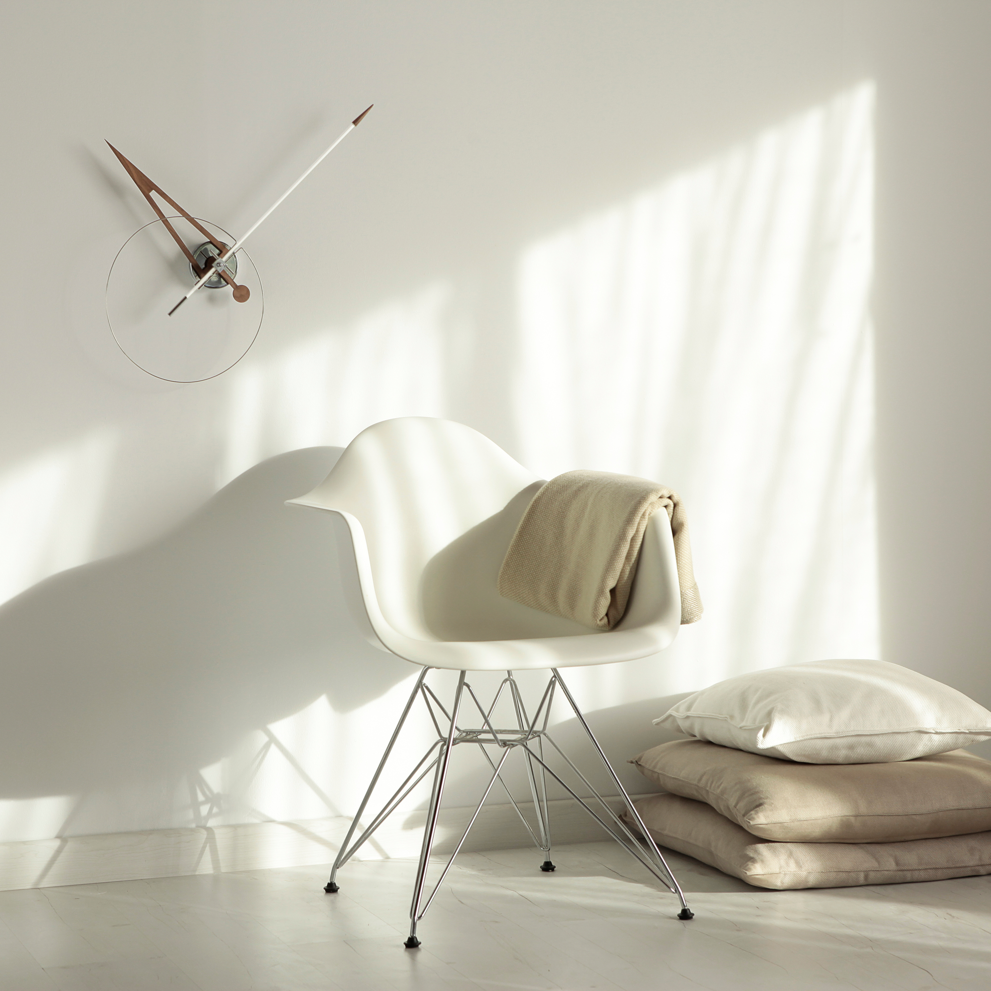 Cris n Wanduhr von Nomon an der Wand über einem Stuhl mit Kissen und Decke.