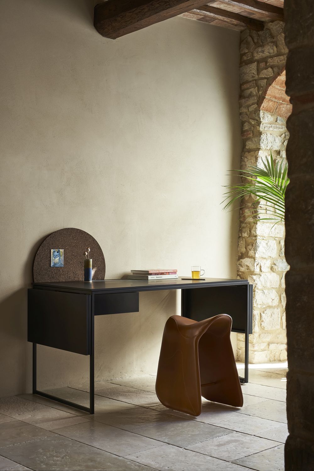 Brauner Pepe Sitzhocker von Opinion Ciatti vor einem schwarzen Schreibtisch in einem stilvollen Raum.