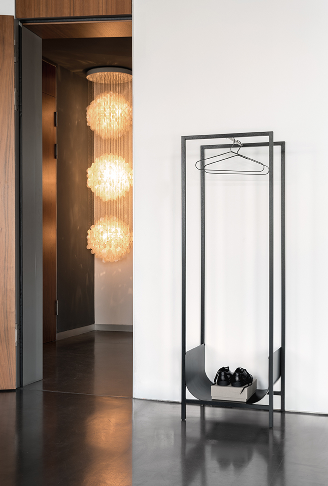 Schönbuch Tub Garderobenständer aus Metall in Schwarz mit Schuhen und Kleiderbügel vor weißer Wand.