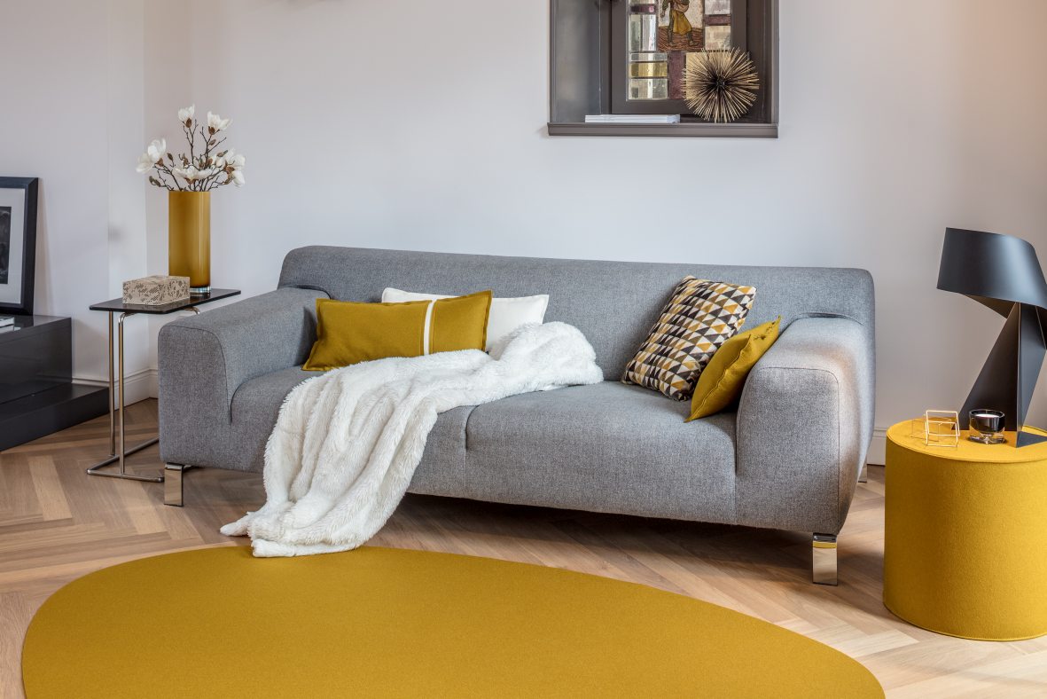 Graues Rondo Sofa von Hey Sign mit gelbem Teppich und Kissen in modernem Wohnzimmer.