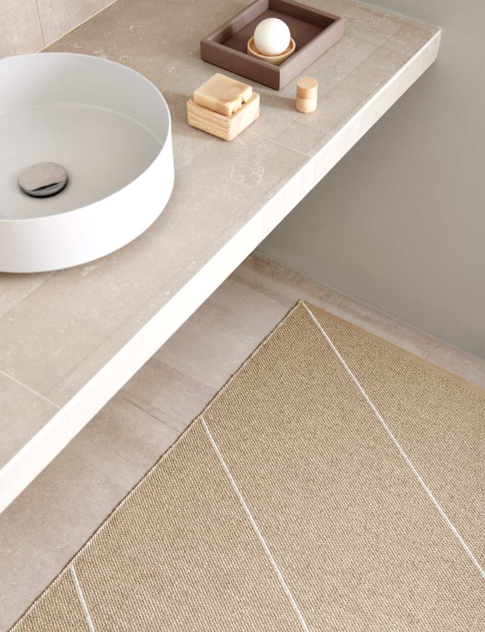 Detailaufnahme: Sandfarbener Randy Kunststoffteppich von Pappelina mit weißen Streifen im Badezimmer.