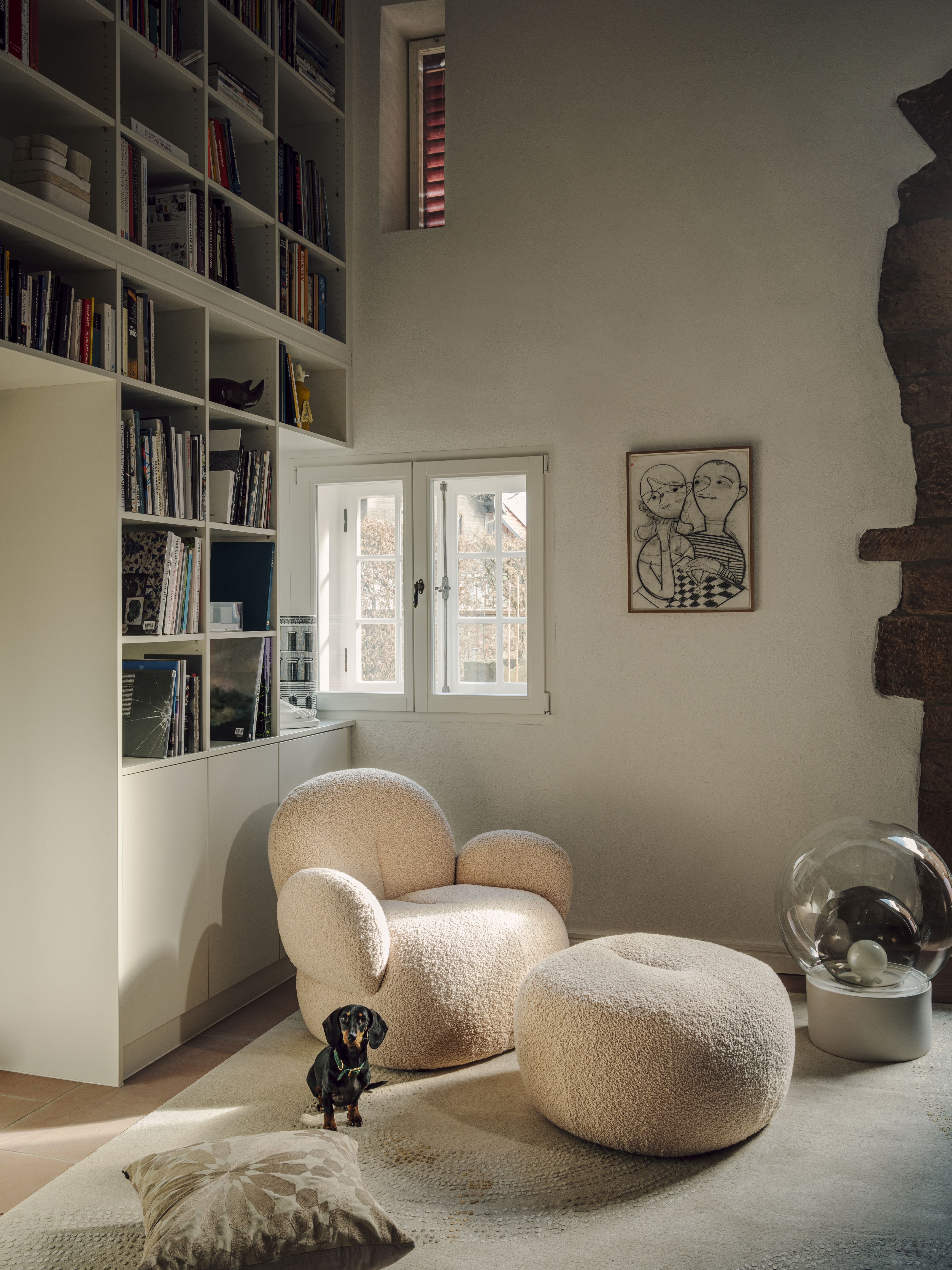 Beiger Nana Love Seat Sessel von Freifrau Manufaktur mit Hocker und Dackel im Wohnzimmer.