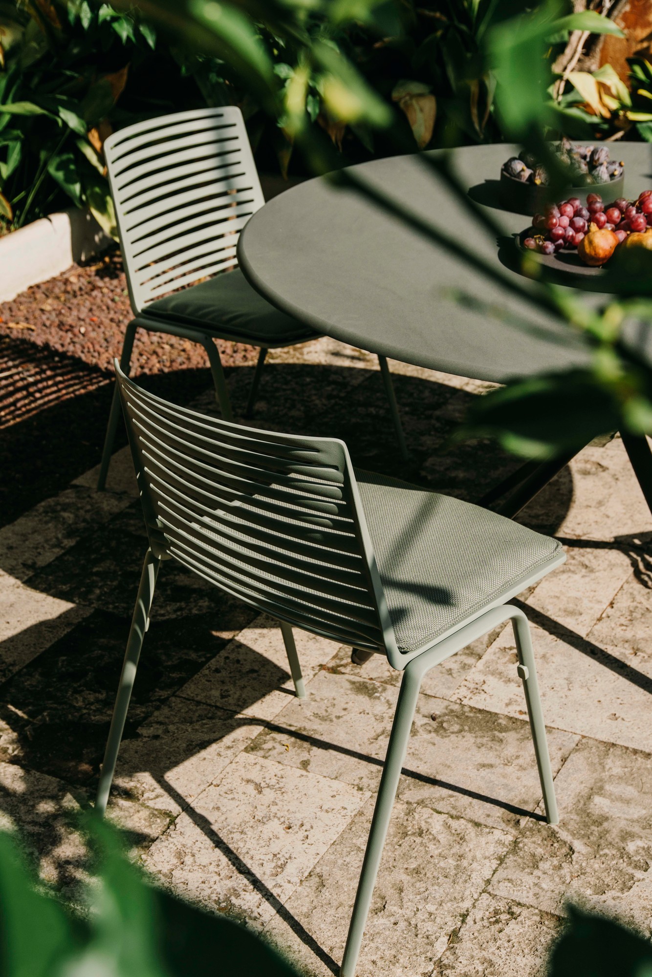 Zwei grüne Zebra Fast Outdoor Stühle und ein Tisch mit Obst im Garten.
