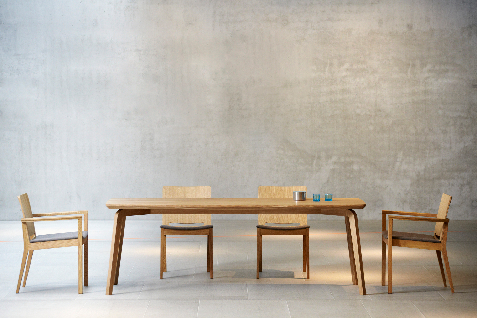 Dweller Tisch von Jan Kurtz mit vier Stühlen aus hellem Holz vor Betonwand.