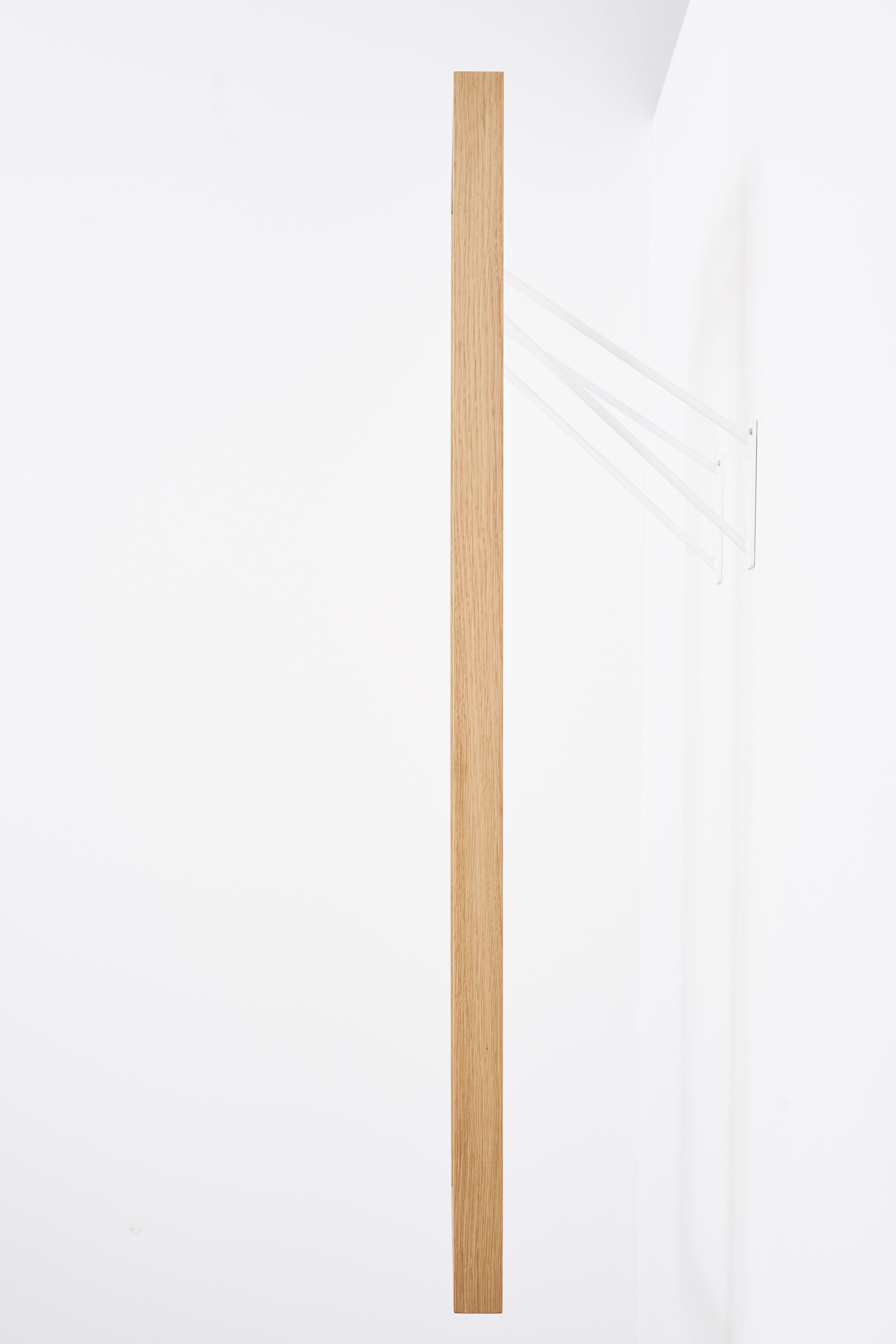 gardero-b Wandgarderobe: Minimalistische Garderobe aus Holz mit weißen, filigranen Aufhängungen an einer weißen Wand.