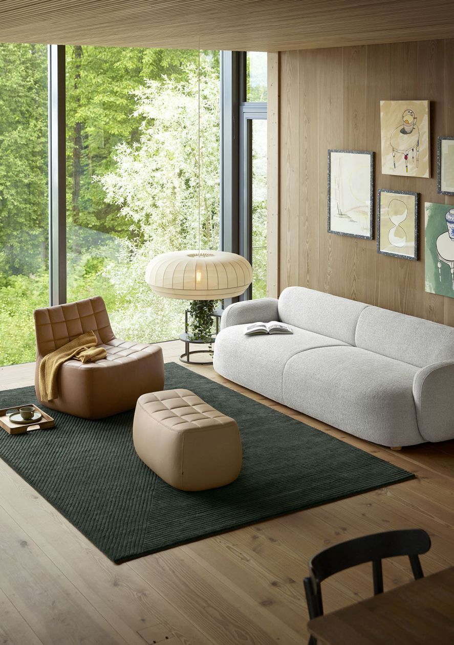 Wohnzimmer mit braunem Gem Sessel, Hocker und hellem Sofa. Skandinavisches Design für gemütliches Wohnen.