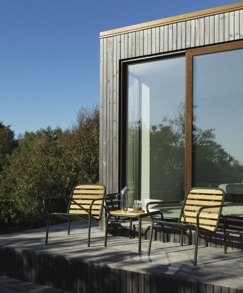 Normann Copenhagen Vig Table Outdoor mit zwei Stühlen auf einer Holzterrasse vor einem modernen Haus.