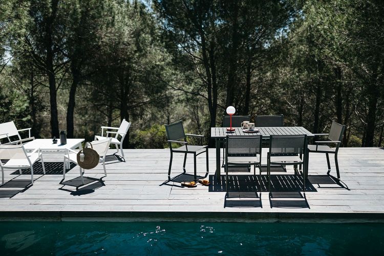 Costa Tisch von Fermob: Schwarzer Gartentisch mit Stühlen auf Holzdeck neben Pool und Bäumen.