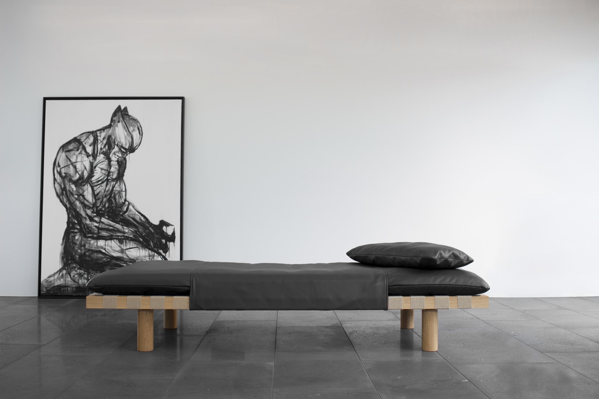 Modernes Paletten Daybed mit grauer Matratze und Kissen vor weißer Wand und Kunstwerk.