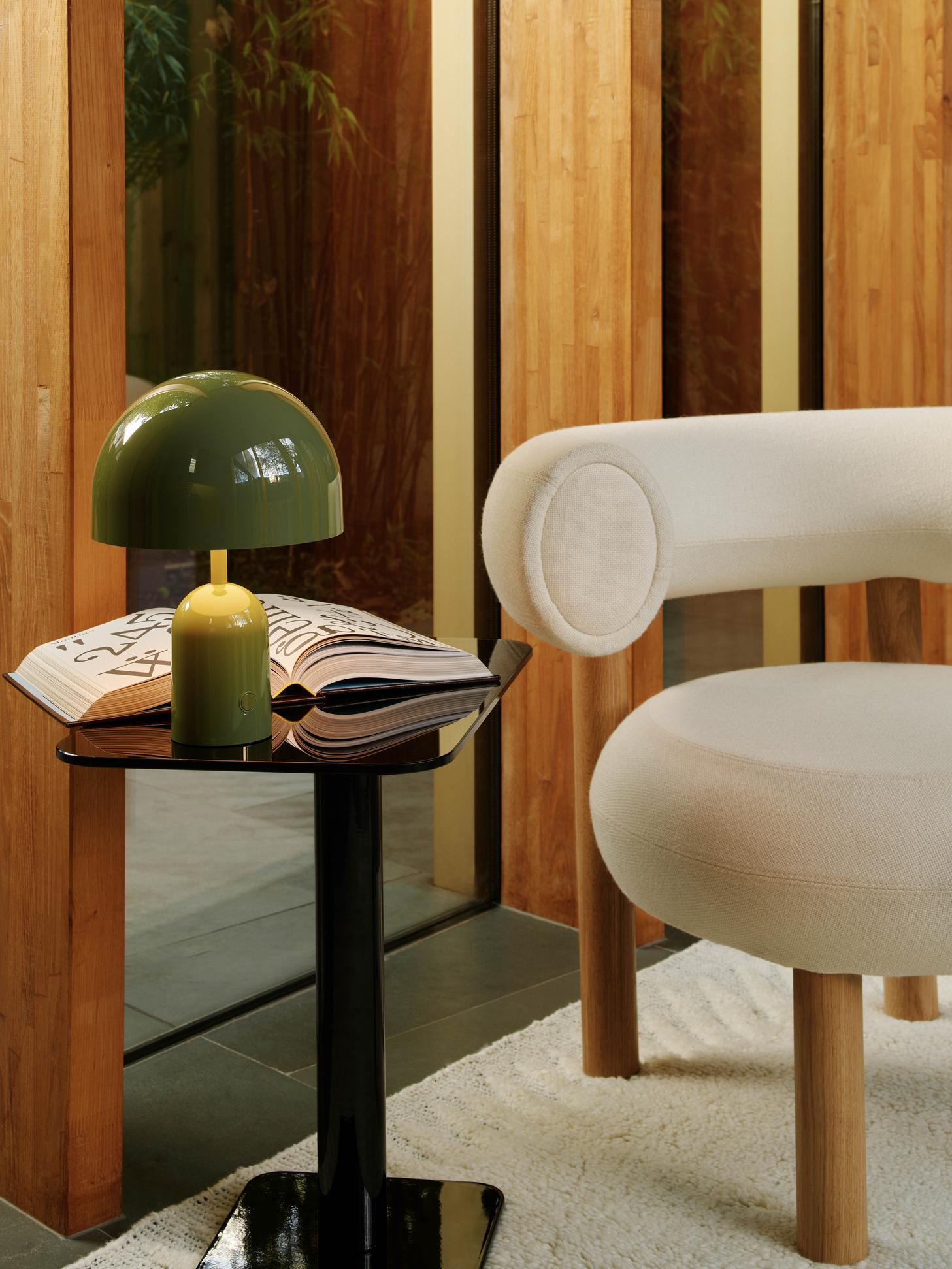 Grüne Bell LED Akkuleuchte von Tom Dixon auf schwarzem Tisch neben Sessel.