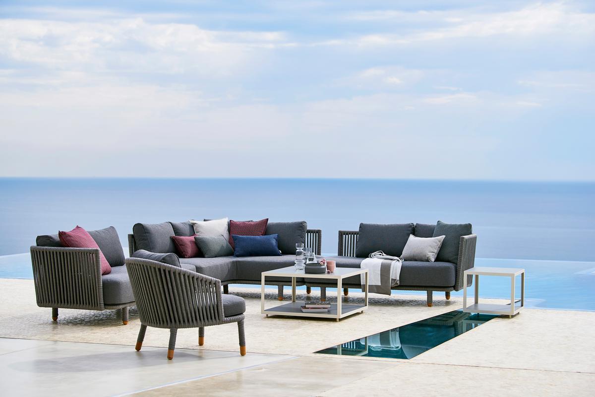 Cane-Line Moments Outdoor Sofa Eckmodul mit Sesseln und Tisch vor Meerblick.
