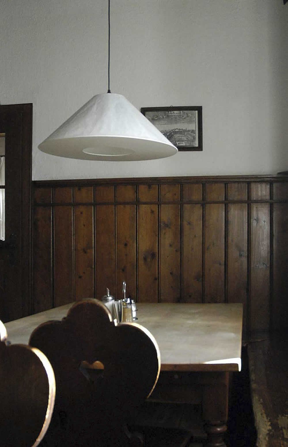 Weiße KNITTERLING Pendelleuchte von Ingo Maurer über einem Esstisch mit Holzvertäfelung.