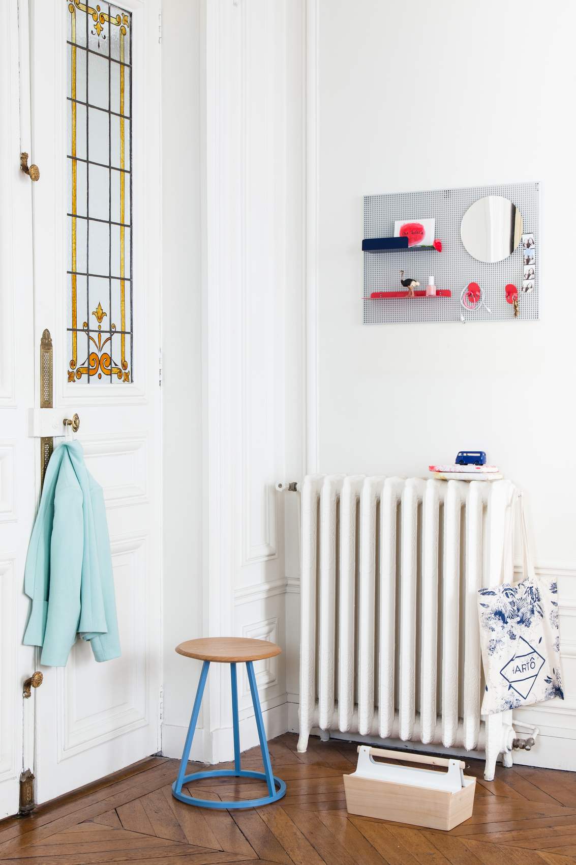 Gustave Hocker von Hartô, ein runder Holzhocker mit blauem Metallgestell in einem hellen Flur.