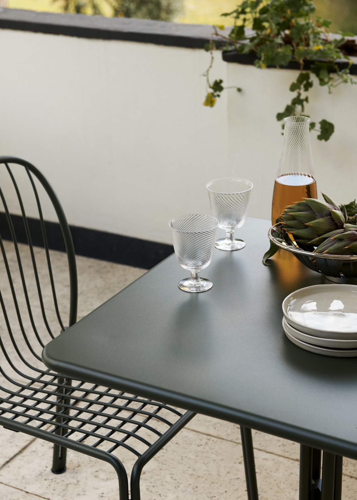 AndTradition Thorvald SC96 Outdoor Tisch in Grün mit Gläsern und Geschirr auf einem Balkon.