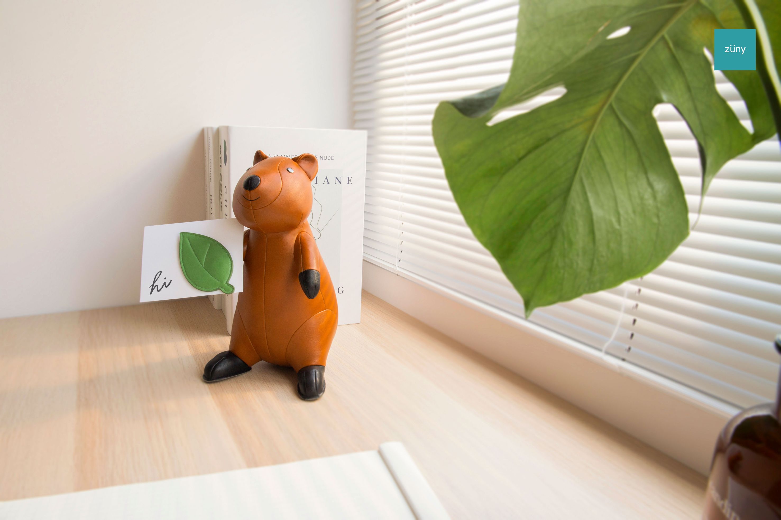 Braune Quokka Buchstütze von Züny hält Bücher auf einem hellen Holztisch. Dekorative Tierfigur.