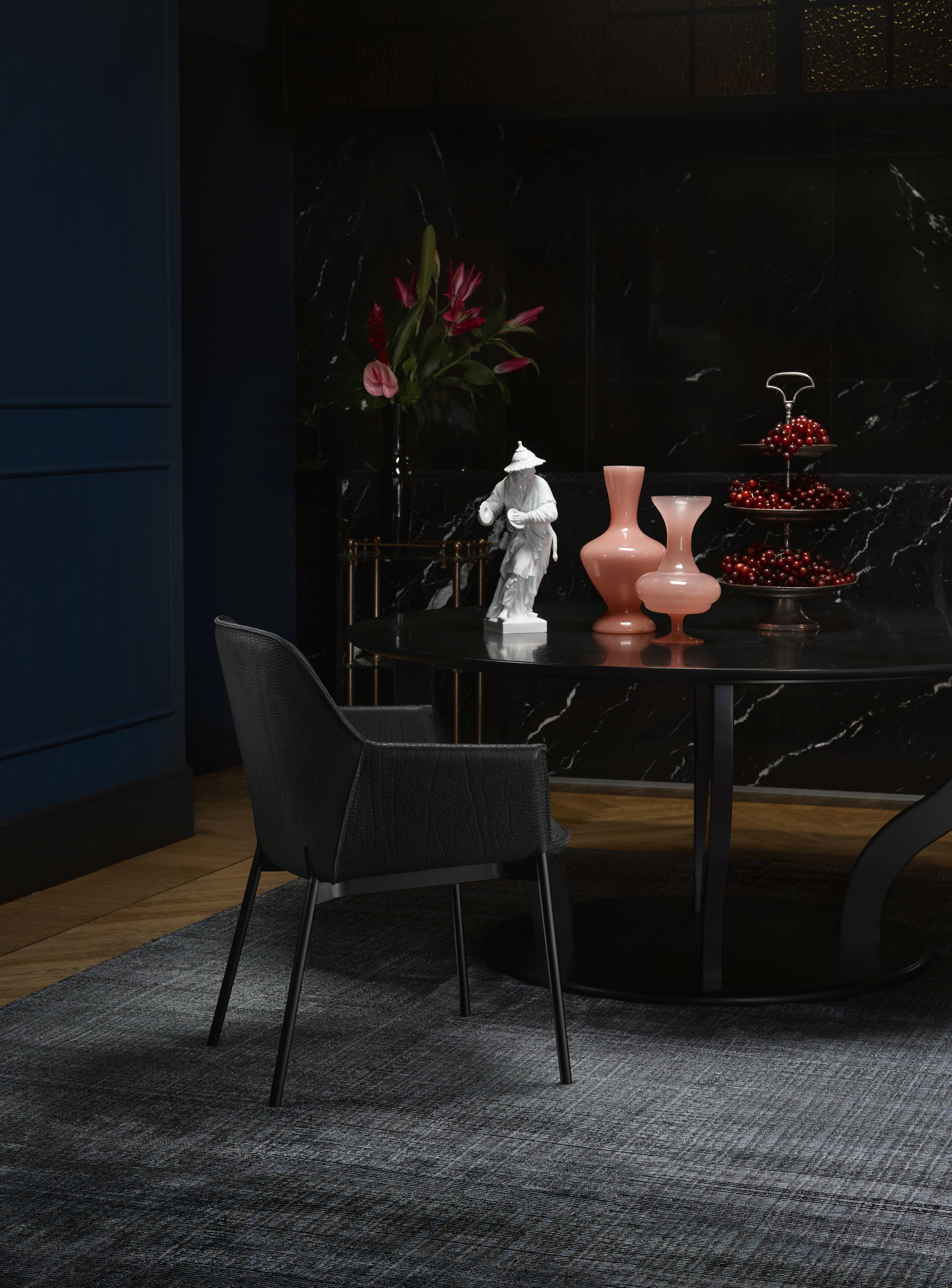 Schwarzer Marla Armlehnstuhl von Freifrau Manufaktur mit hohen Armlehnen vor dunklem Hintergrund. Design Stuhl für Esszimmer.