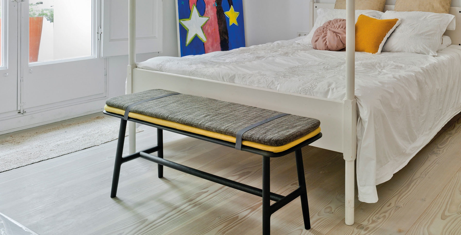 Nudo Sitzbank von Sancal mit grauem Bezug und gelbem Kissen vor einem Bett.
