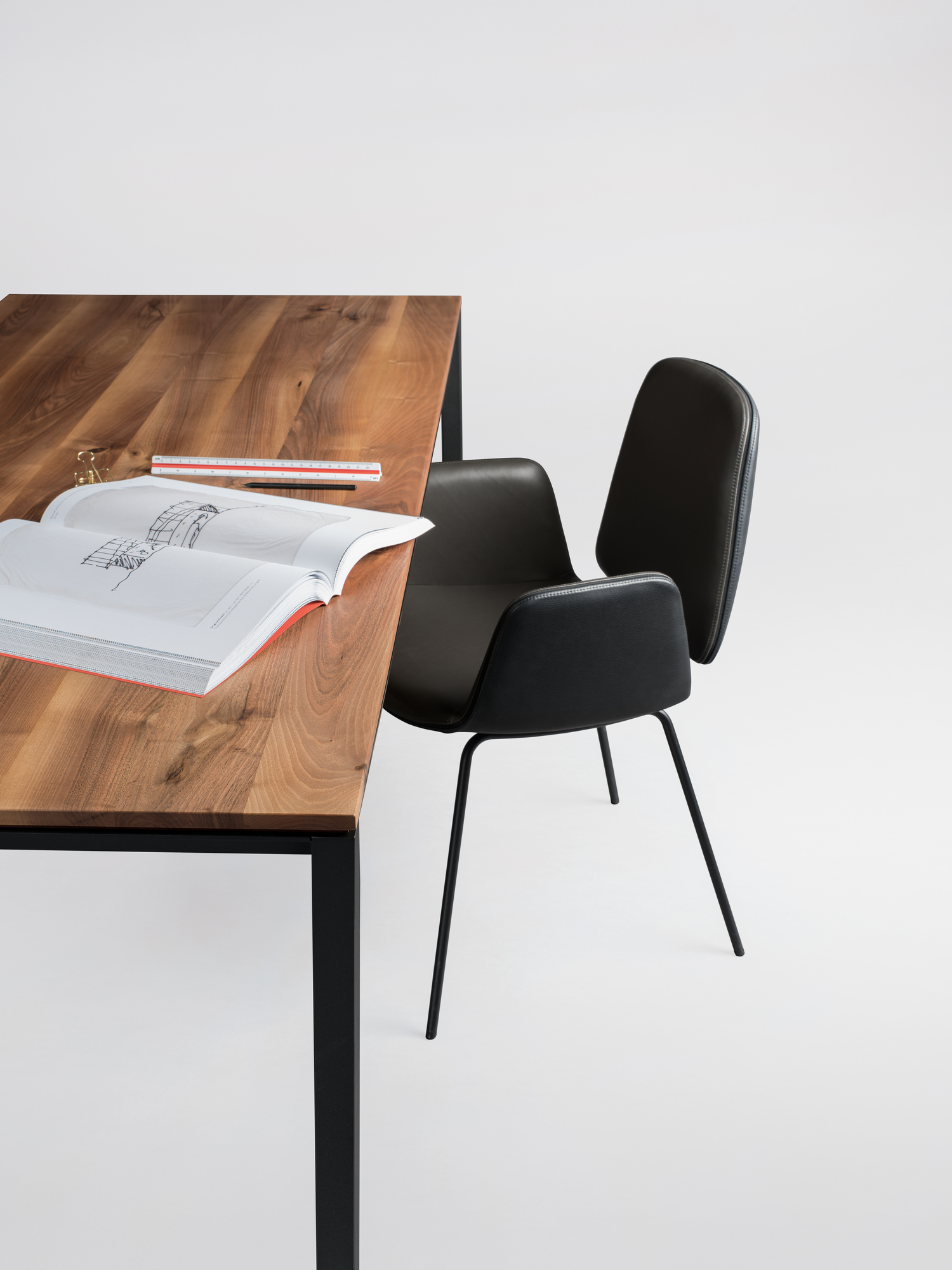 Janua S 600 Tisch mit Nussbaumplatte und schwarzem Stahlgestell, daneben ein schwarzer Stuhl.