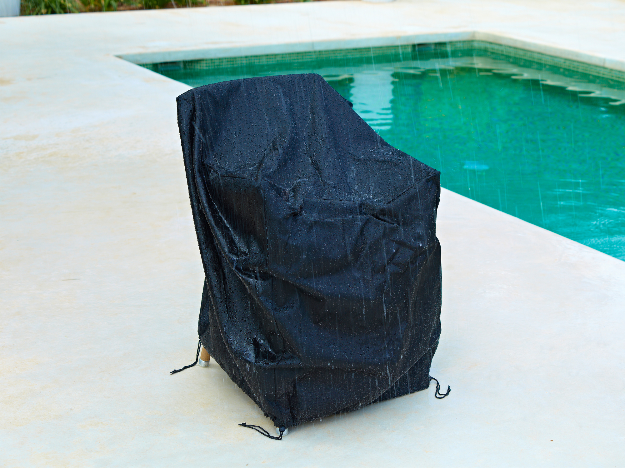 Schwarze Cane-Line Schutzhülle für große Outdoor Sofa Möbel, wasserabweisend und langlebig, neben einem Pool.