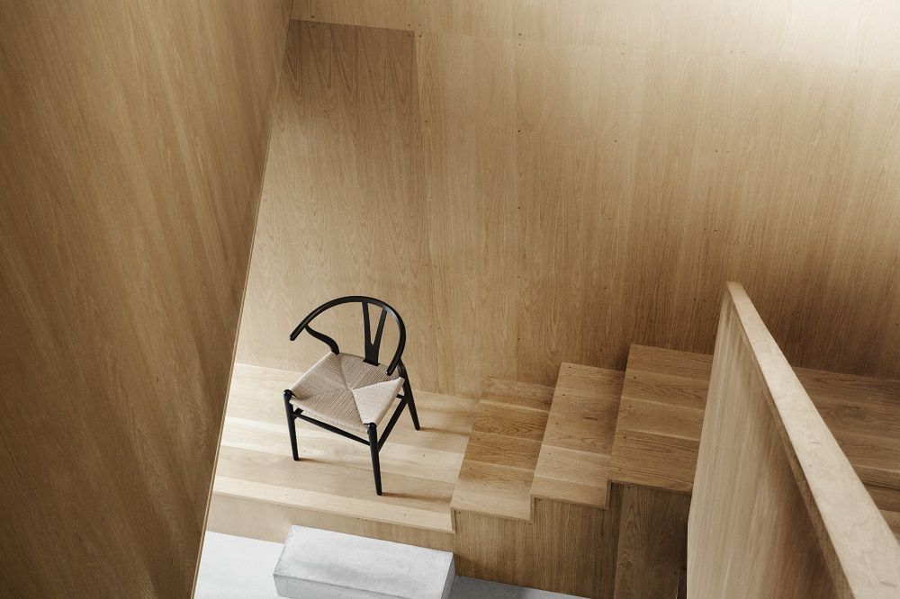 CH24 Wishbone Chair mit schwarzem Gestell und heller Sitzfläche auf Holztreppe, minimalistisches Design.