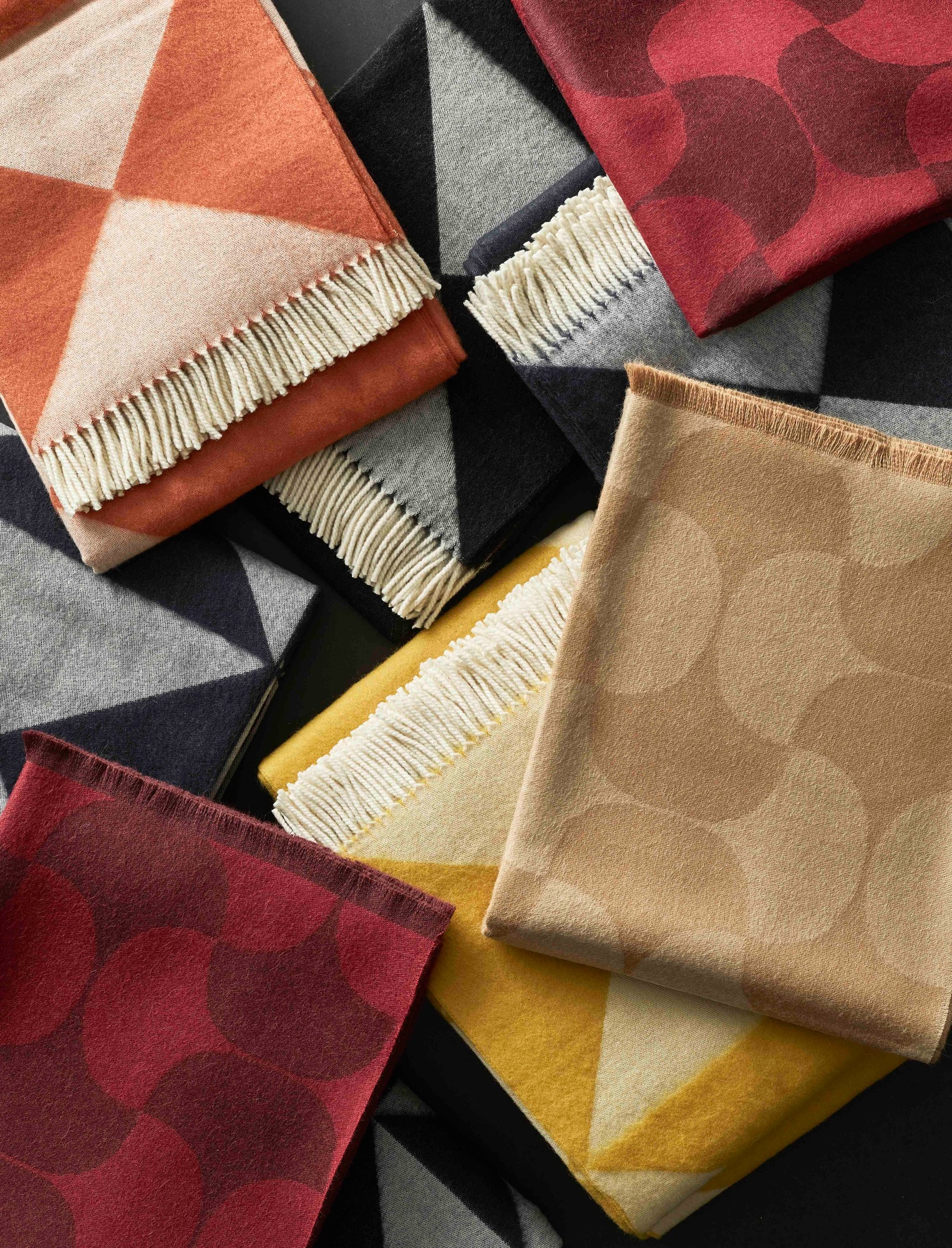 Nahaufnahme von mehreren Verpan Überwürfen, darunter der orangefarbene Mirror Throw mit Fransen. Dekorative Wohndecke für Sofa oder Bett.