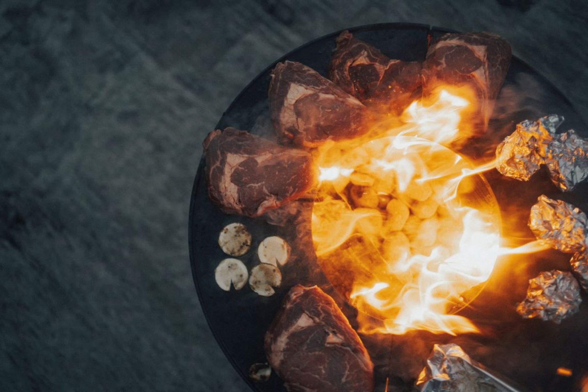 Grill mit saftigen Steaks, Kartoffeln und Folienkartoffeln über offenem Feuer. Perfekt für ein BBQ.