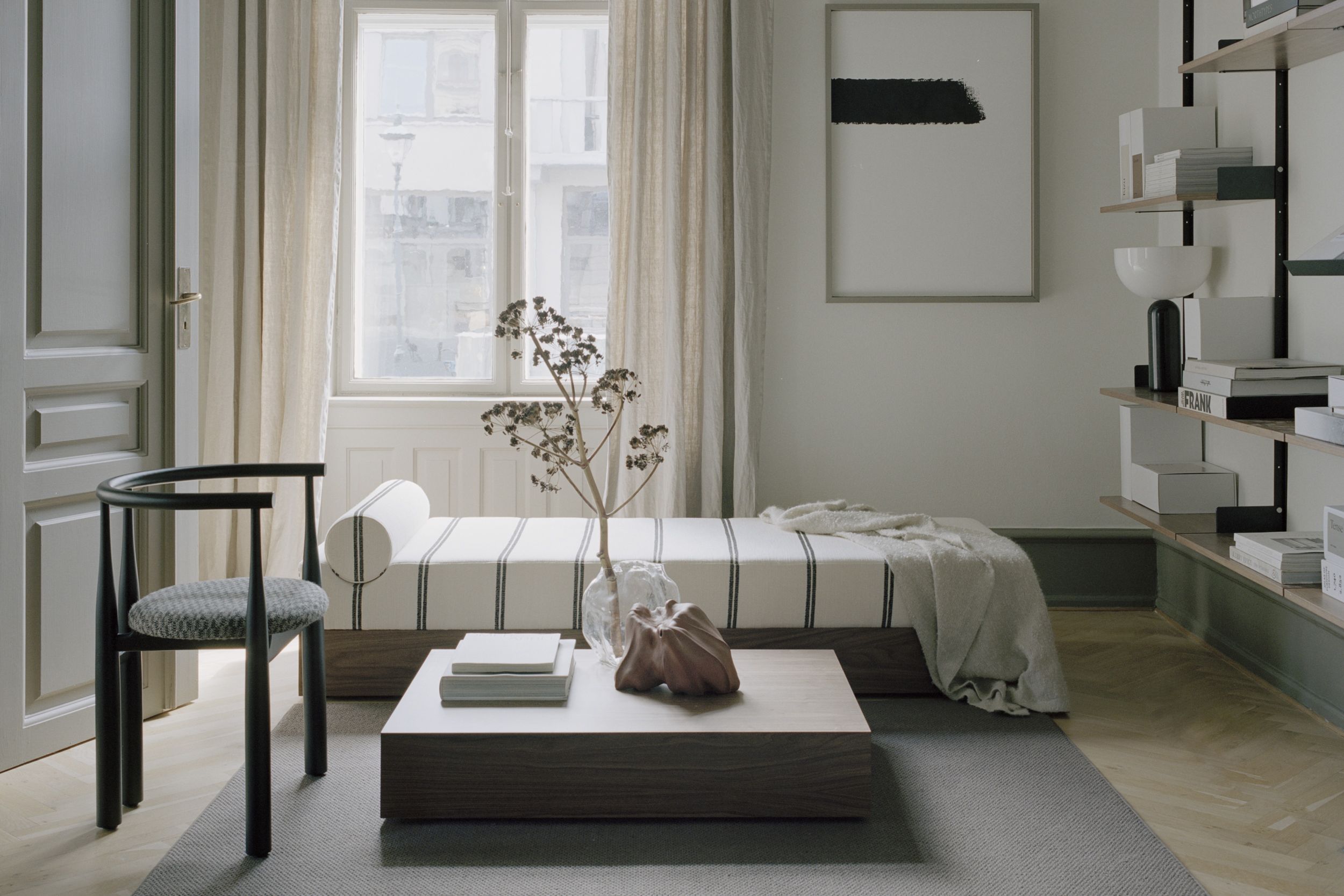 Wohnzimmer mit Mass Tagesbett Ohio, schwarzem Holzstuhl, Couchtisch und minimalistischer Dekoration.