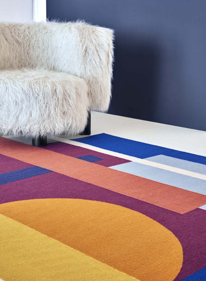 Detailansicht des Zoe Sool Teppichs von Gan mit geometrischen Formen und farbenfrohem Design neben einem Sessel.