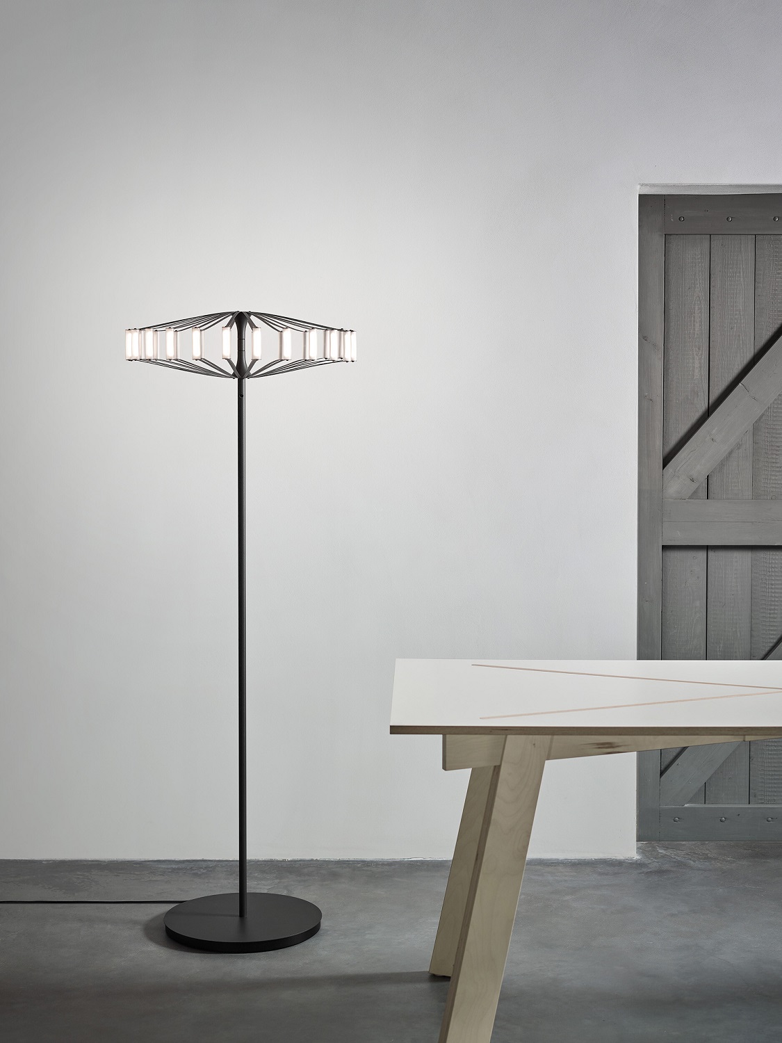 Moderne Wheel Floor Stehleuchte Japth in Schwarz mit geometrischem Lampenschirm und warmweißem Licht, neben Holztisch.