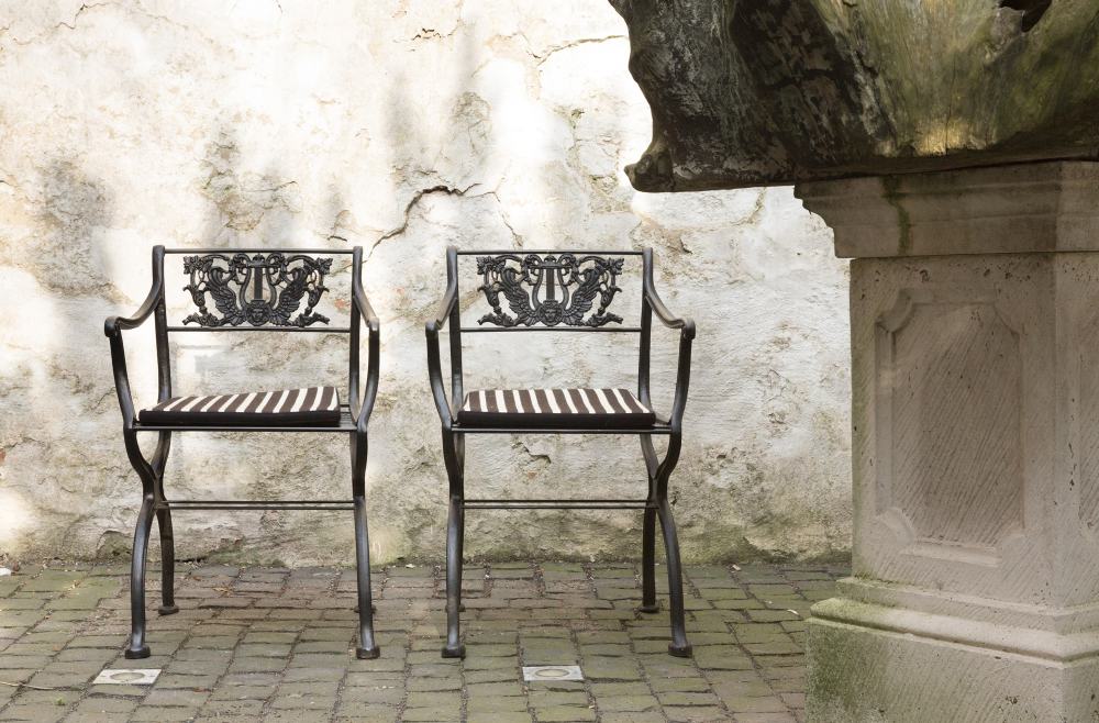 Zwei D60 Tecta Gartensessel aus Metall mit gestreiften Sitzkissen vor einer alten Mauer.