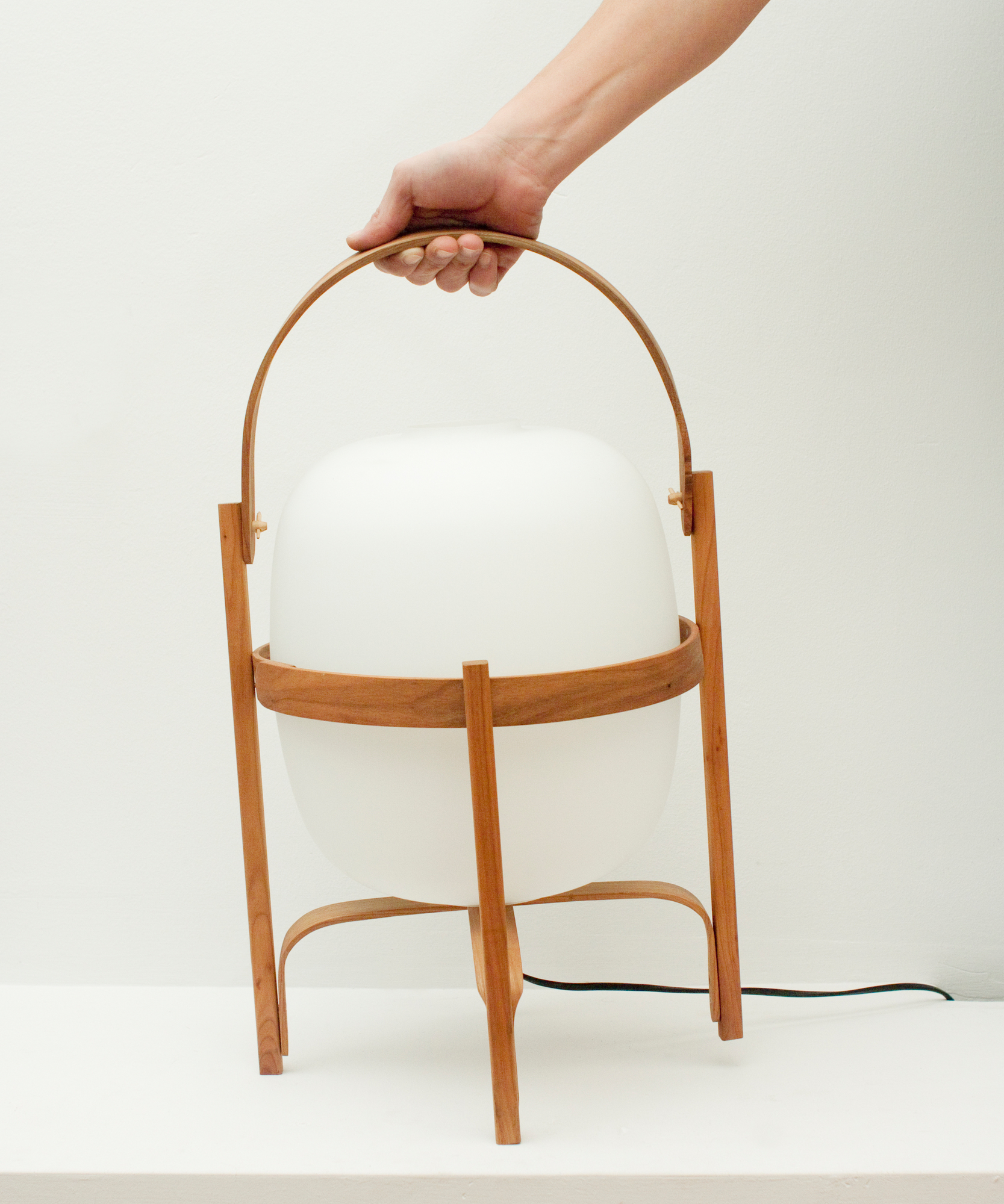 Hand hält Cesta Tischleuchte von Santa & Cole. Moderne Tischlaterne mit Holzgestell und weißem Lampenschirm.