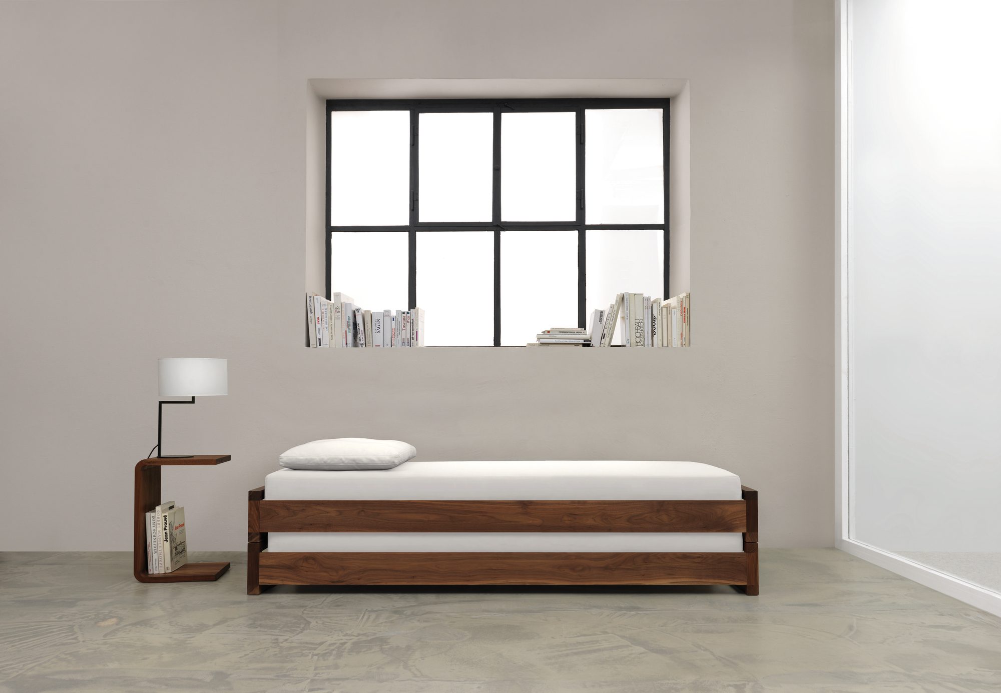 Waitress Beistelltisch aus Nussbaumholz neben einem minimalistischen Bett mit weißer Matratze und Lampe.