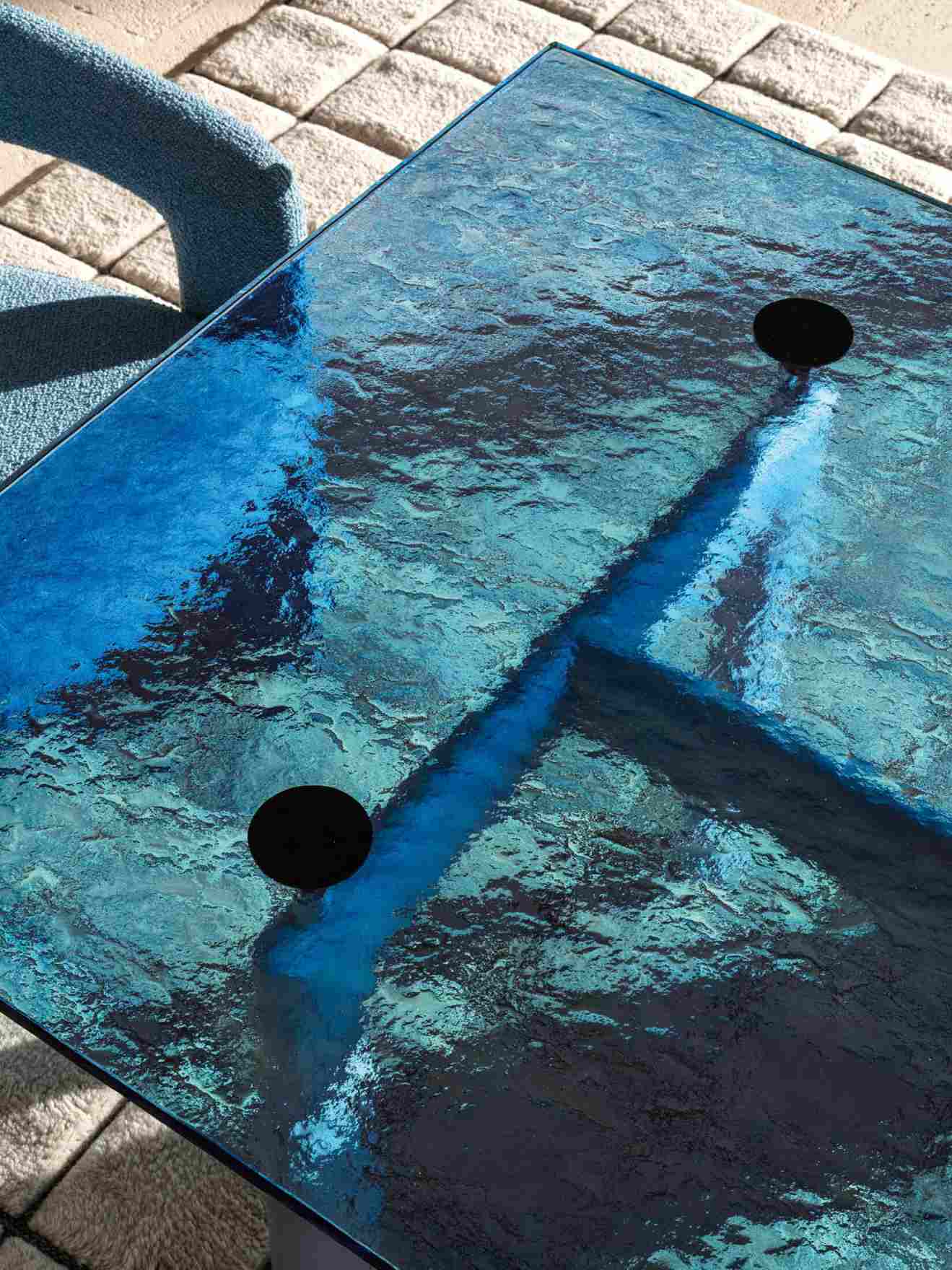 Detailaufnahme des Cassina LC6 Esstisches mit blauem Glasplatte und schwarzen Bohrungen, modernes Design.