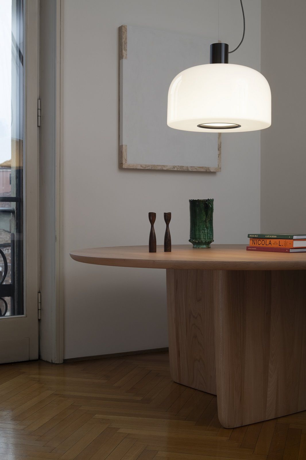 Nahaufnahme der Bellhop Glass Pendelleuchte von Flos über einem Holztisch.