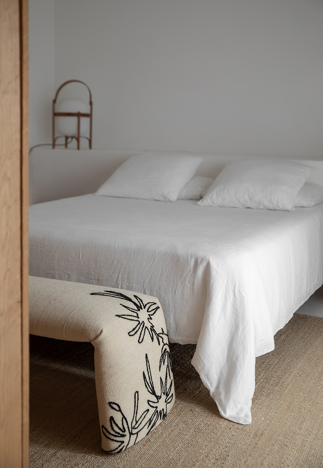 Beige Bank mit Blumenmuster vor weißem Bett, Nanimarquina Bankhocker für Schlafzimmer.