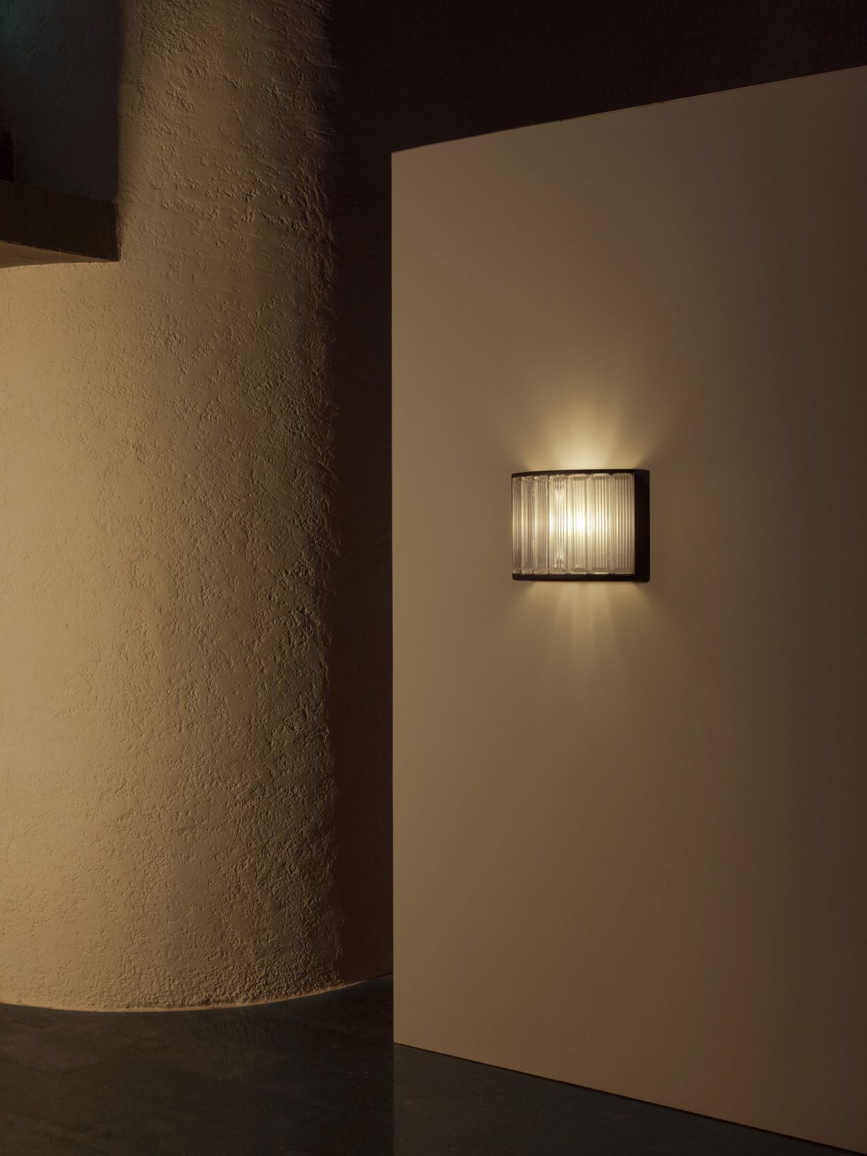 Estadio Wandleuchte von Santa & Cole an beiger Wand, modernes Design, warmes Licht.