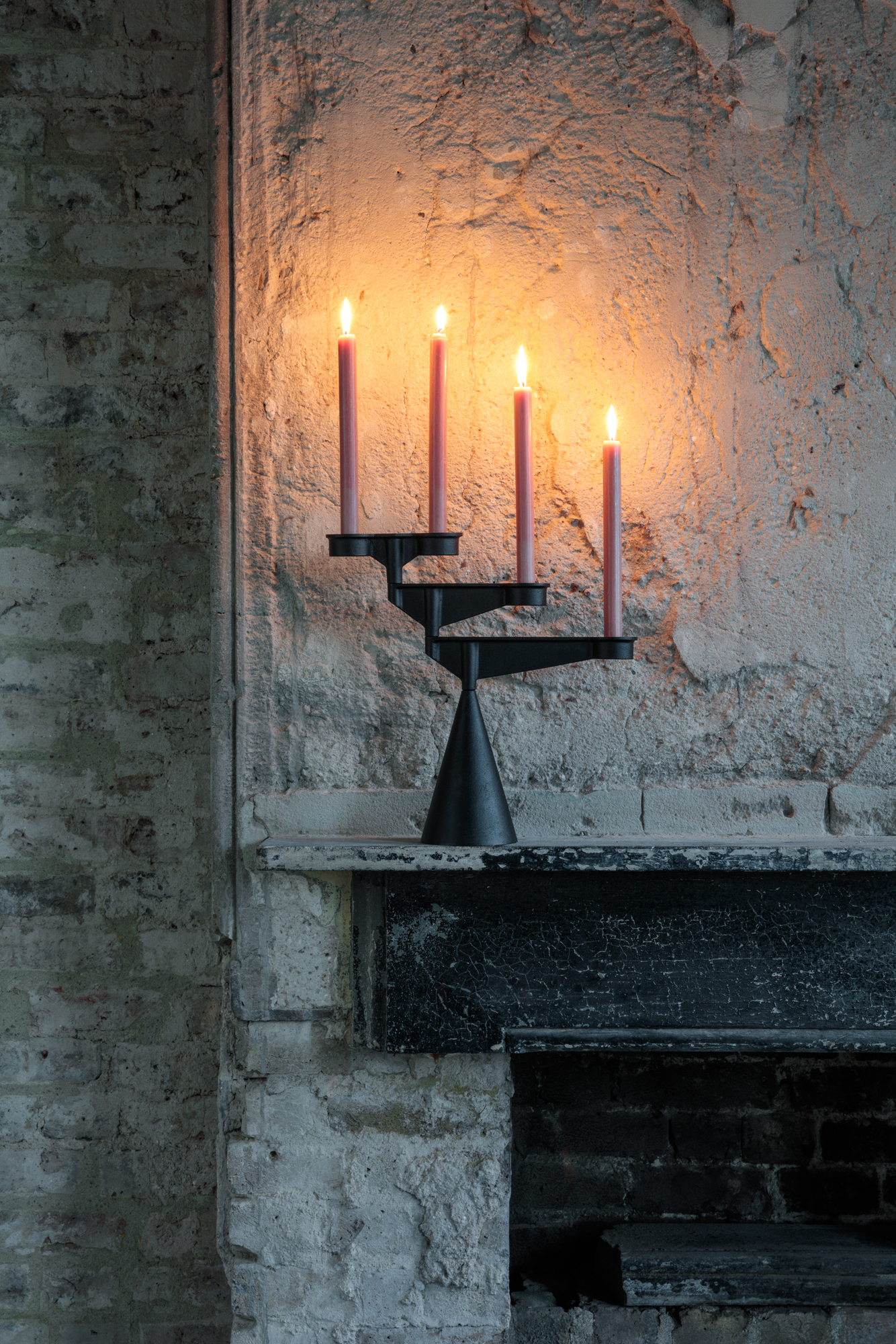 Schwarzer Spin Candelabra Kerzenständer mit vier brennenden, rosa Kerzen vor einer Backsteinwand. Tom Dixon Design.