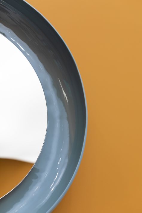 Detailaufnahme: Coque Spiegel von Miniforms mit blauem Keramikrahmen vor ockerfarbenem Hintergrund.