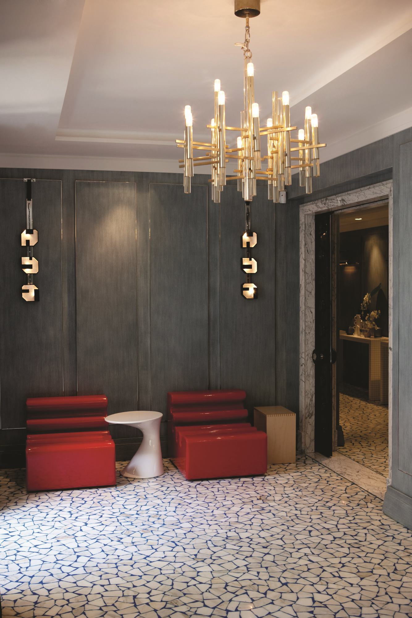 Elegantes Interieur mit roter Sitzgruppe und weißem Zanotta Tod Couchtisch unter einem goldenen Kronleuchter.