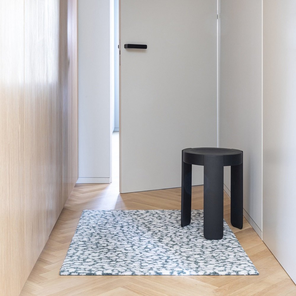 Heymat Grain Granite Fußmatte im Flur, kombiniert mit einem schwarzen Hocker auf Parkettboden.