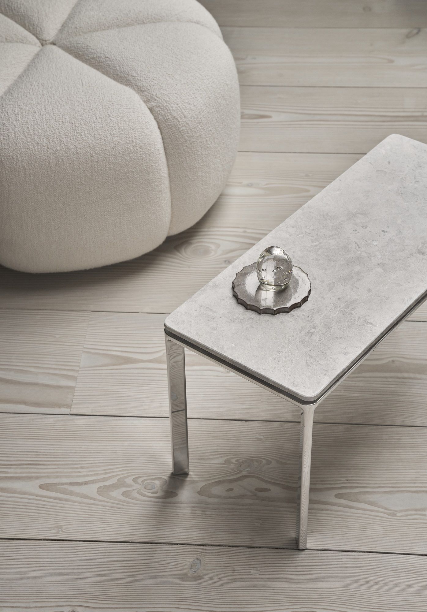 Rechteckiger Vipp Couchtisch mit Marmorplatte und Deko-Objekt, neben einem runden, weißen Sitzhocker.
