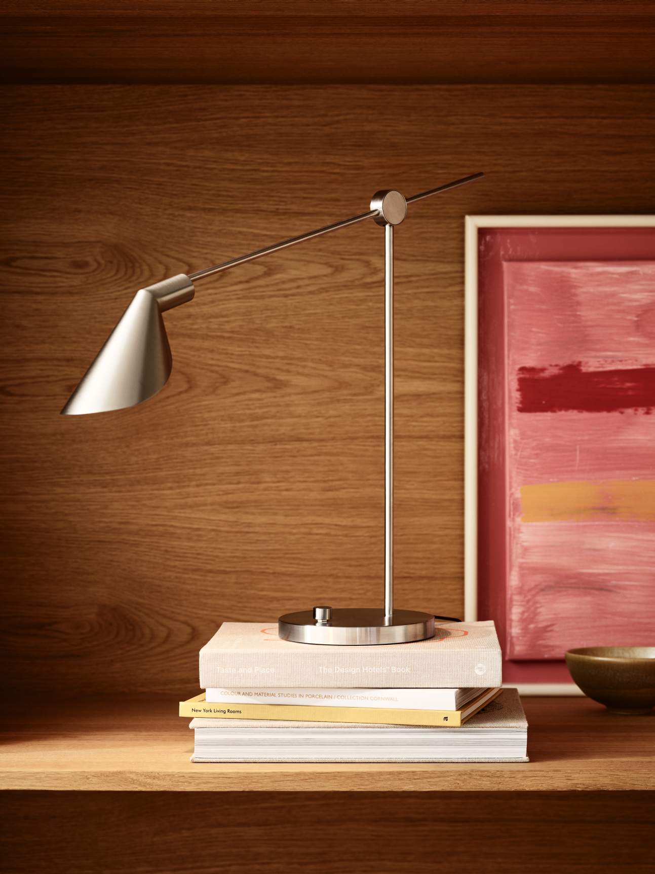 Silberne MS Series Tischleuchte von Fritz Hansen auf Bücherstapel vor Holzregal. Designlampe.