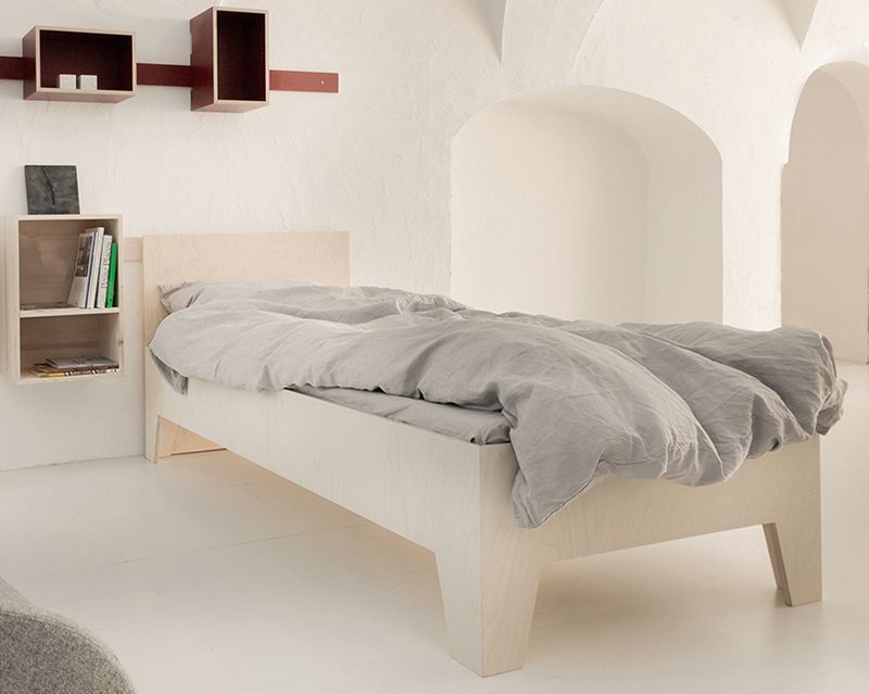 Helles Schlafzimmer mit modernem Holzbett und grauer Bettwäsche, inklusive Nachttisch und Wandregalen.