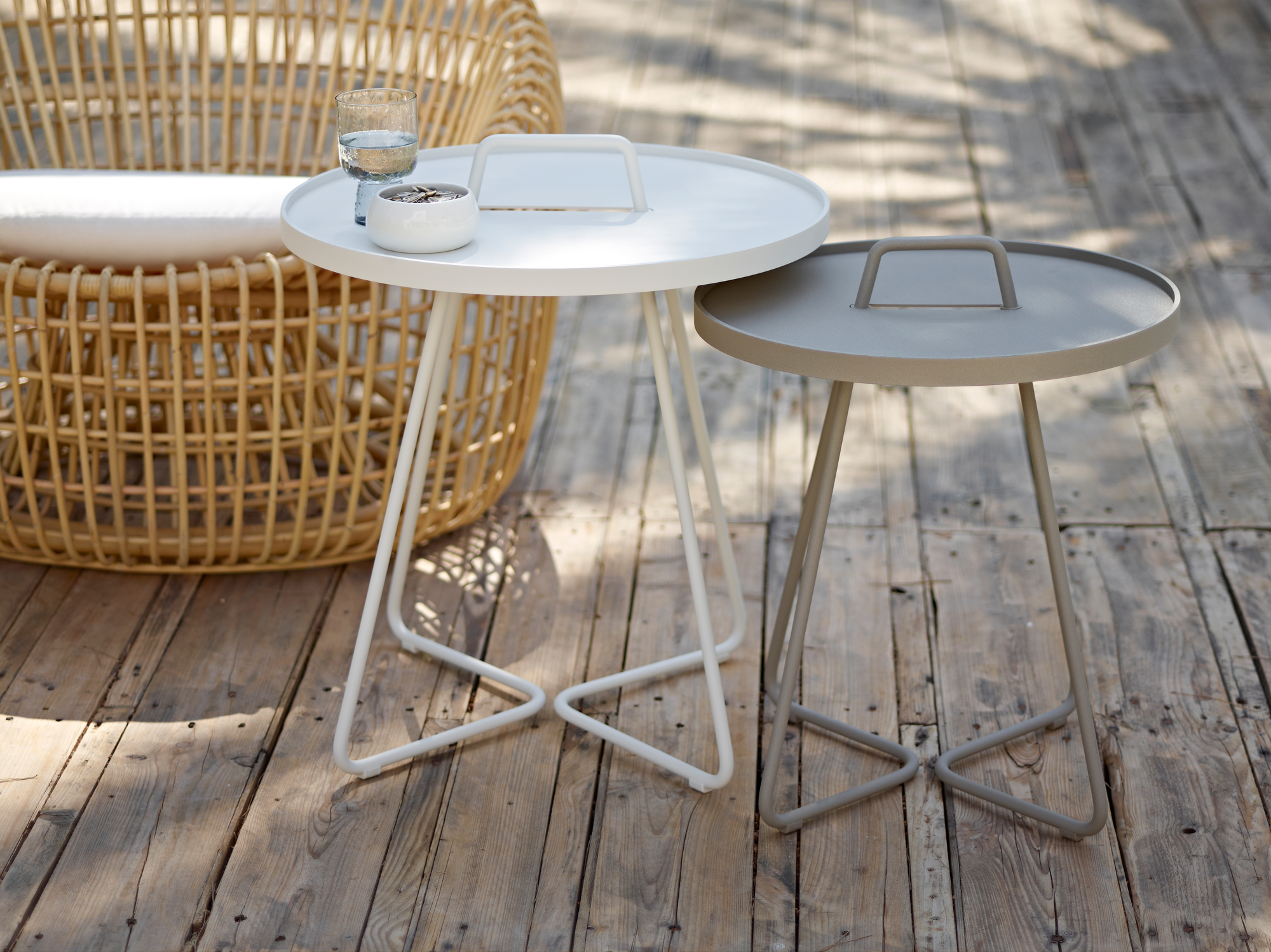 Zwei Cane-Line On-The-Move Beistelltische in Weiß und Grau auf einer Holzterrasse.