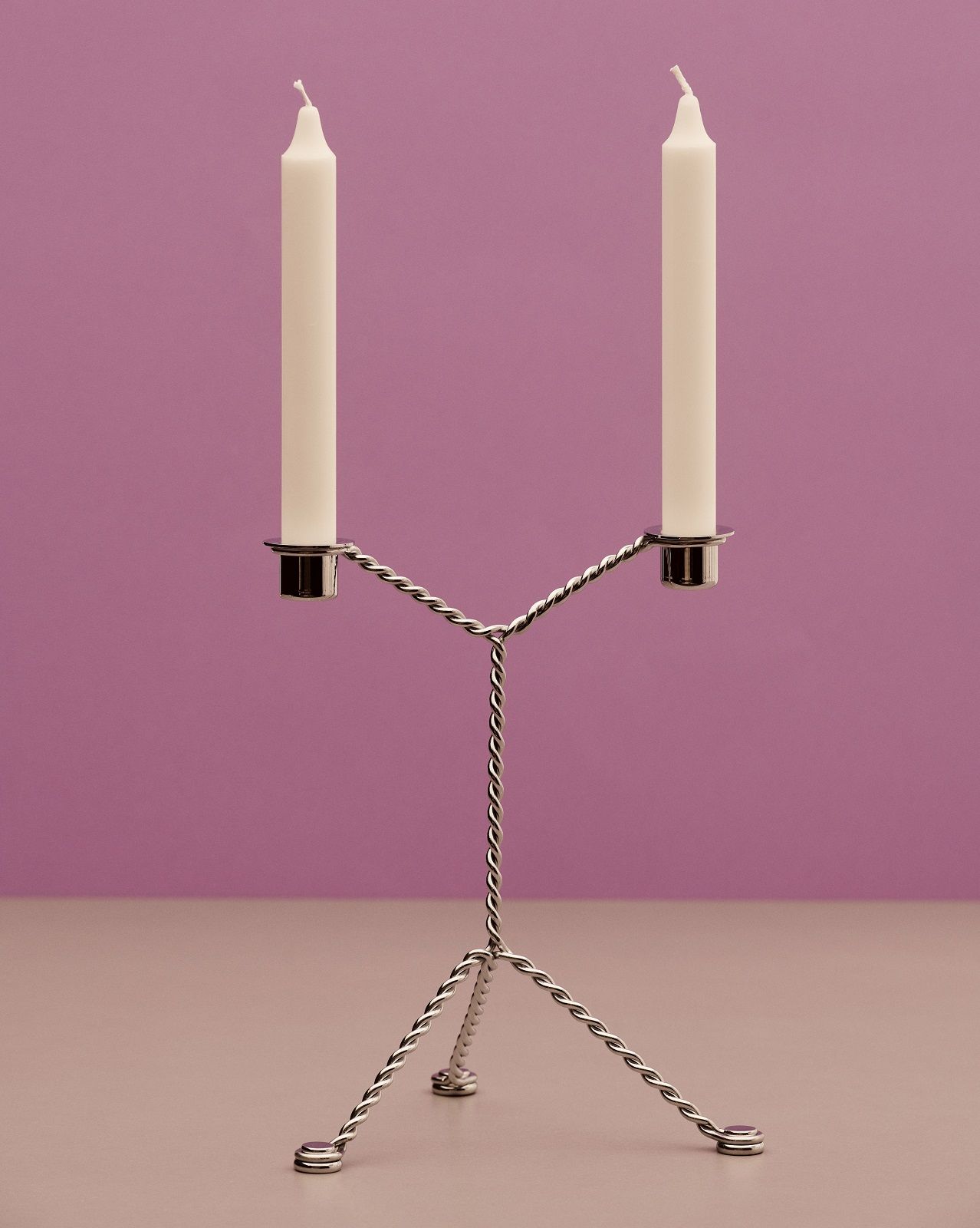 Hay Wire Candleholder: Moderner, silberner Kerzenständer für zwei Stabkerzen vor lila Hintergrund.
