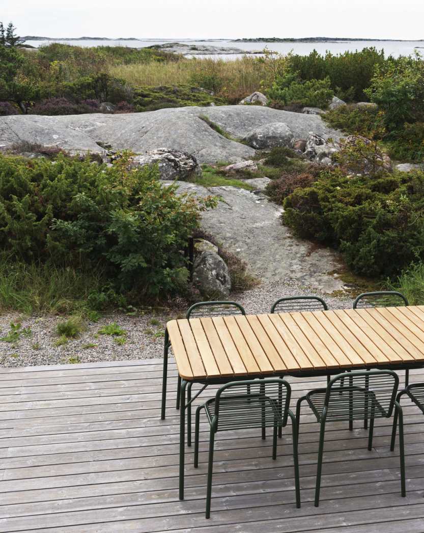 Normann Copenhagen Vig Chair Outdoor und Holztisch auf Holzterrasse mit Blick auf Felsen und Vegetation.